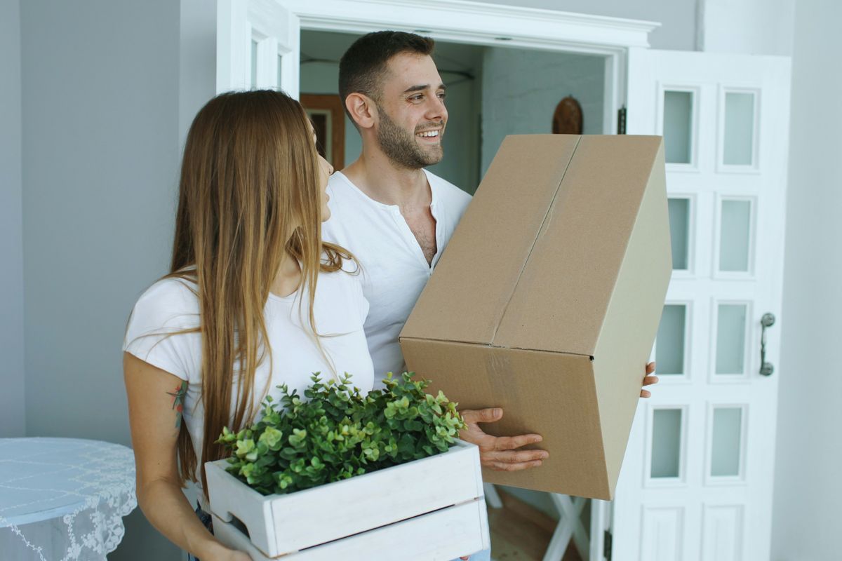 Couple carrying moving boxes into a new home